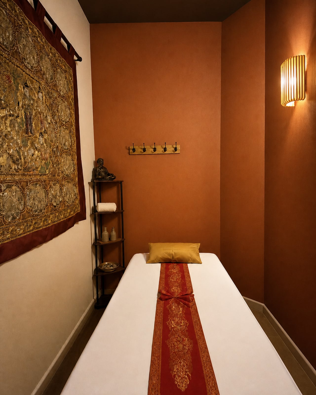Cabine de massage HOOM aux murs terracotta avec tenture brodée, étagère de soins et linge crème.