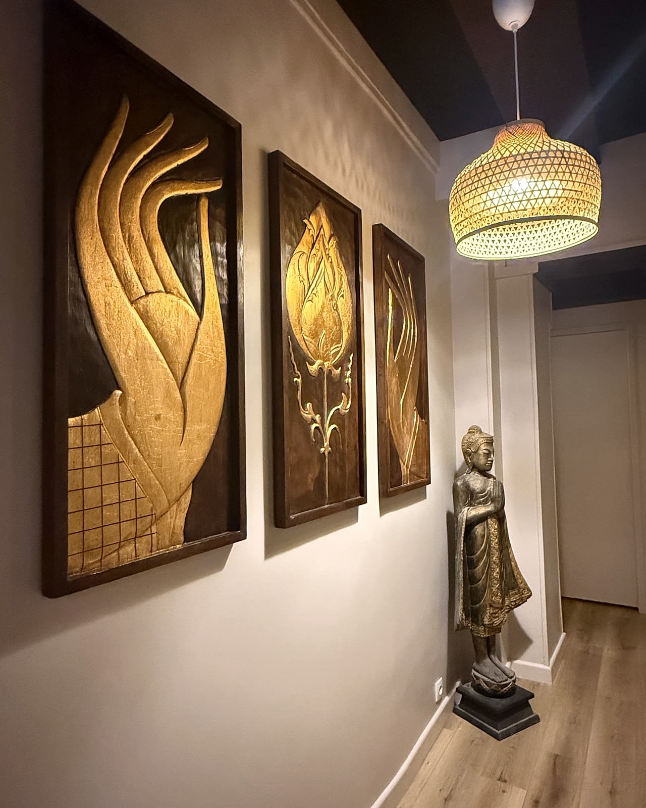 Couloir HOOM décoré de trois panneaux dorés, d'une statue et d'une suspension en rotin.
