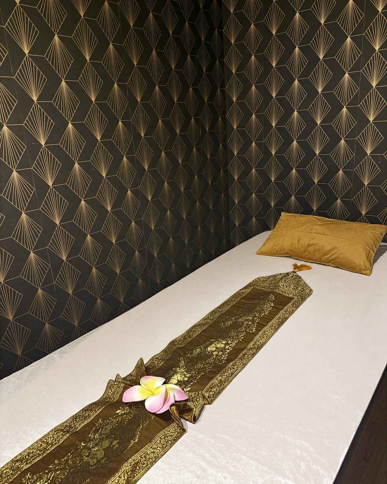 Détail d'une table de massage devant un papier peint géométrique noir et doré.
